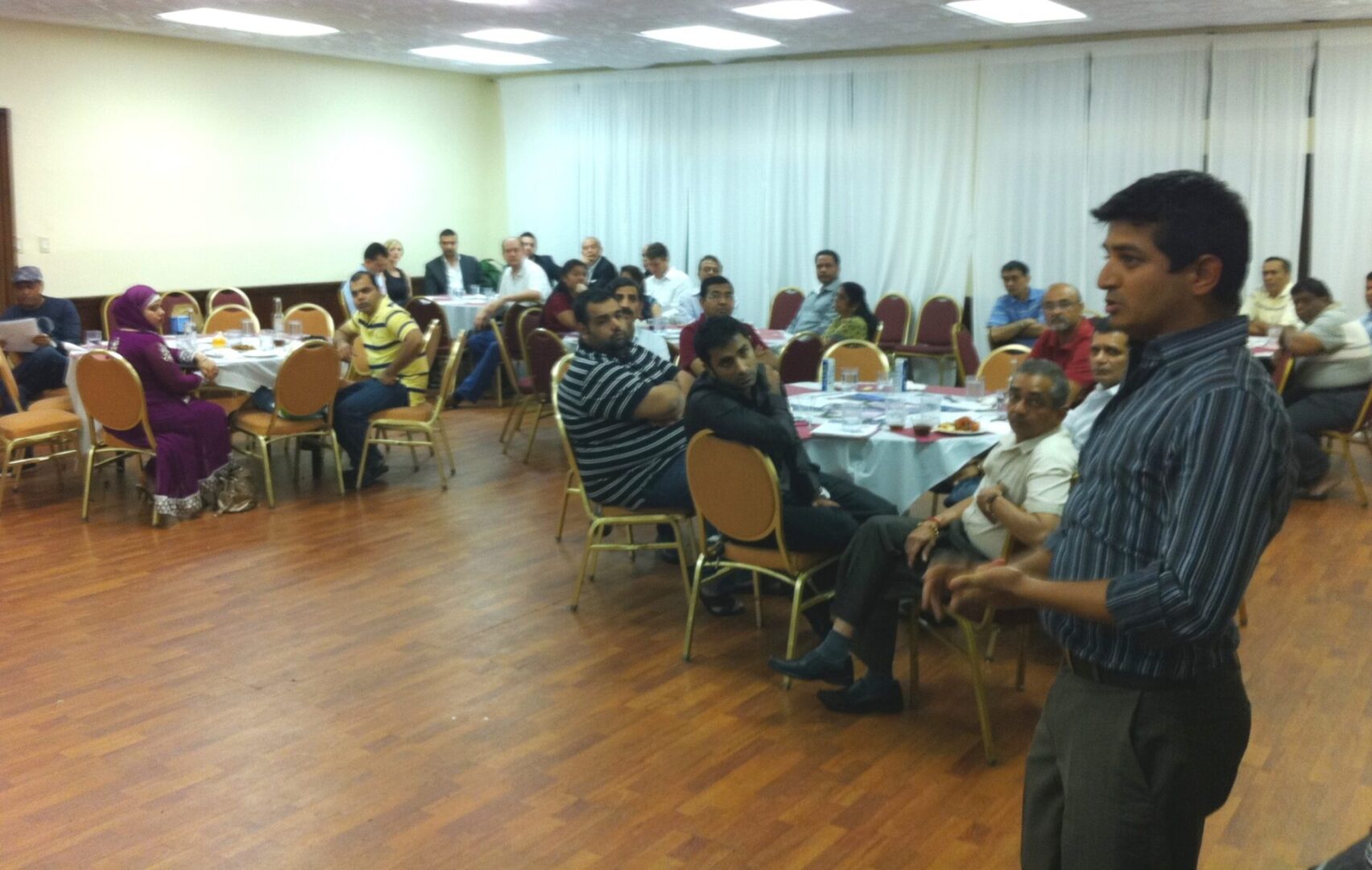 A group of people sitting at tables in front of a wall.